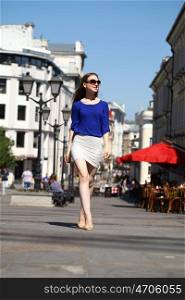 Young beautiful girl in a blue blouse and white skirt walks down the street