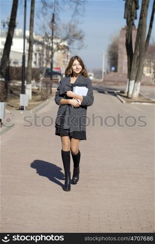 Young beautiful girl in a gray coat walking down the street