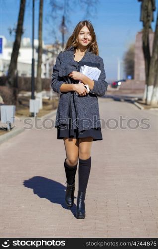 Young beautiful girl in a gray coat walking down the street