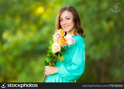 Young beautiful girl in a long dress walking in the woods on a warm summer day. Portrait of a girl with a bouquet of roses on the background blurred foliage