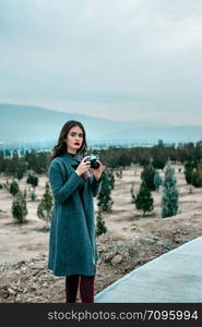 young beautiful girl in Burgundy stockings and gray coat stands with vintage camera at sunset