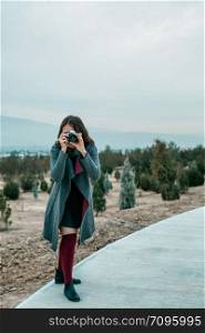 young beautiful girl in Burgundy stockings and gray coat stands with vintage camera at sunset