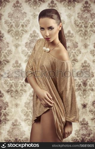 Young, beautiful girl in sparkling gold dress and beautiful, big, gold necklace. She wears purple strong make up and she is looking at camera.