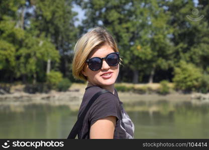 Young beautiful girl in sunglasses against the background of river landscape, portrait of blonde.. Young beautiful girl in sunglasses against the background of river landscape, portrait of blonde