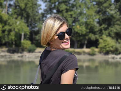 Young beautiful girl in sunglasses against the background of river landscape, portrait of blonde.. Young beautiful girl in sunglasses against the background of river landscape, portrait of blonde