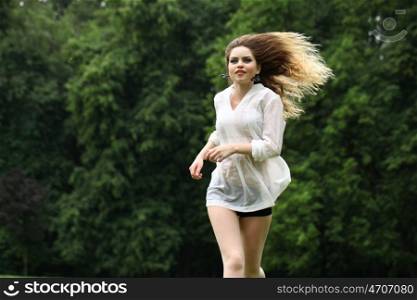 Young beautiful girl in the white shirt is running on the green field in summer park