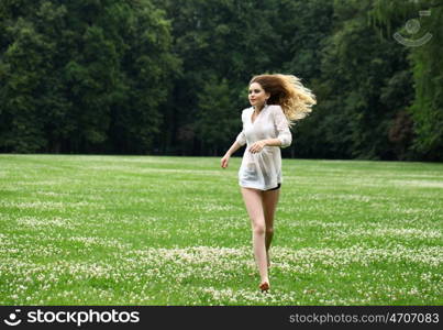 Young beautiful girl in the white shirt is running on the green field in summer park