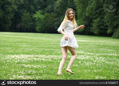 Young beautiful girl in the white shirt is running on the green field in summer park