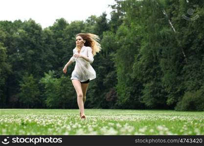 Young beautiful girl in the white shirt is running on the green field in summer park