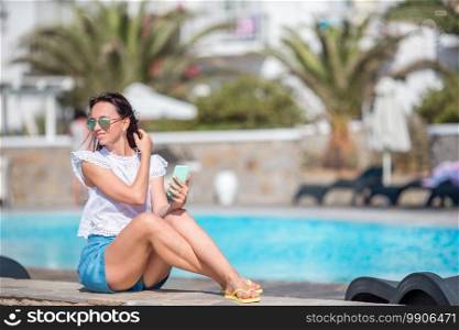 Young beautiful girl on the edge of swimming pool at summer vacation. Young beautiful girl taking selfie