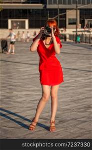 Young beautiful girl photographer in a bright red dress focuses on a model with a large digital camera. beautiful girl photographer
