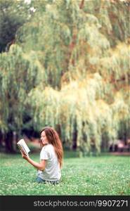 Young beautiful girl reading a book in the park outdoors. Relaxed young woman reading book