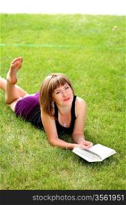 Young beautiful girl reading in the park laying on the grass