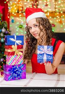 Young beautiful girl sitting at a table with Christmas gifts in the Christmas atmosphere. She has prepared gifts for loved ones