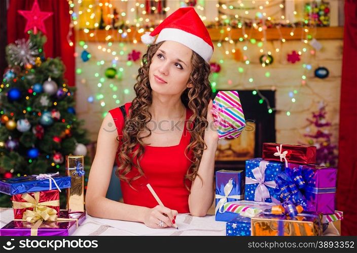 Young beautiful girl sitting at a table with Christmas gifts in the Christmas atmosphere. Beautiful girl who thought to give a gift