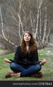 Young beautiful girl sitting on the grass and meditates