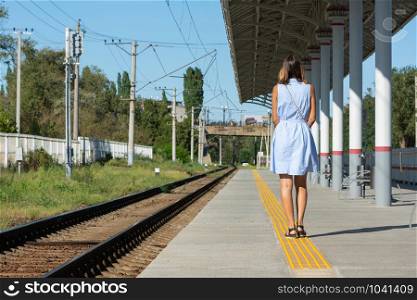 Young beautiful girl stands alone on a railway platform with her back to the camera