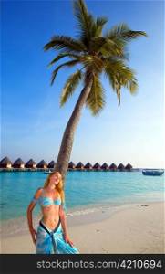 Young beautiful girl stands near by palm tree on background of ocean, Maldives