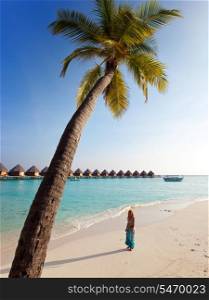 Young beautiful girl stands near by palm tree on background of ocean, Maldives