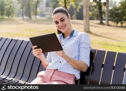 Young beautiful girl using tablet while sitting on the park bench