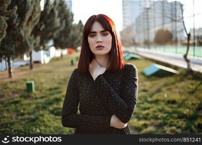 young beautiful girl with heavy and sullen look in black dress outside posing during sunset
