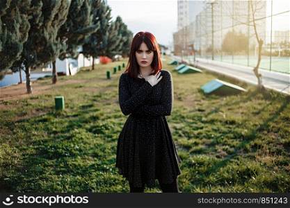 young beautiful girl with heavy and sullen look in black dress outside posing during sunset