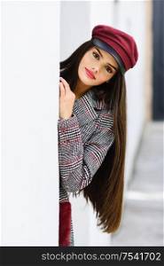 Young beautiful girl with very long hair looking at camera wearing winter coat and cap outdoors. Lifestyle and fashion concept.. Beautiful girl with very long hair wearing winter coat and cap outdoors.