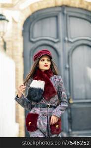 Young beautiful girl with very long hair looking away wearing winter coat and cap outdoors. Lifestyle and fashion concept.. Young beautiful girl with very long hair looking away wearing winter coat and cap outdoors.