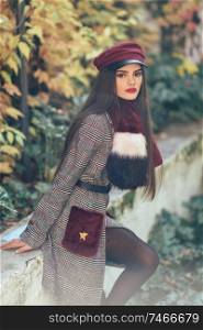 Young beautiful girl with very long hair wearing winter coat and cap in autumn leaves background. Lifestyle and fashion concept.. Young beautiful girl with very long hair wearing winter coat and cap in autumn leaves background