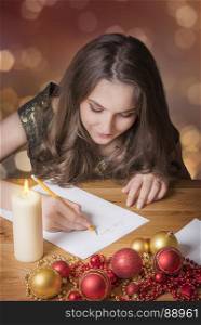 Young beautiful girl writing to Santa Claus, at candlelight, surrounded by colorful globes and other Christmas decorations.