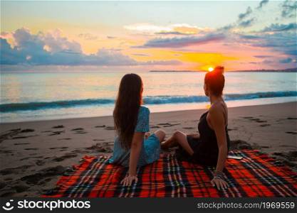 Young beautiful girls relaxing on the beach at sunset. Women on the beach enjoying summer holidays looking at the sea