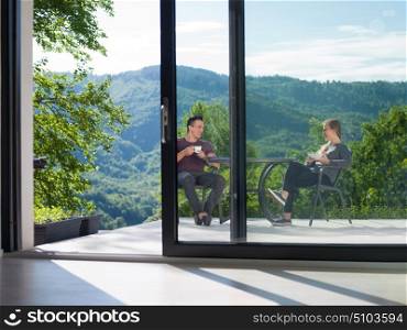 young beautiful handsome couple enjoying morning coffee and breakfast in front of their luxury home villa