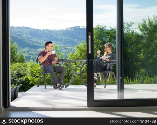 young beautiful handsome couple enjoying morning coffee and breakfast in front of their luxury home villa