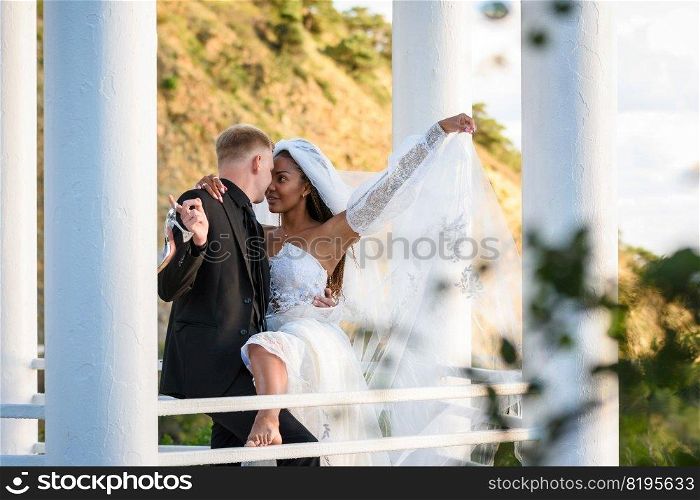 Young beautiful interracial newlyweds hugging in the gazebo