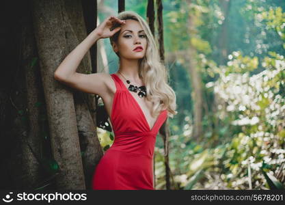 Young beautiful lady in red dress in tropical forest