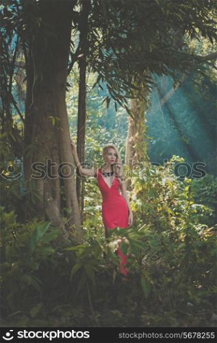Young beautiful lady in red dress in tropical forest