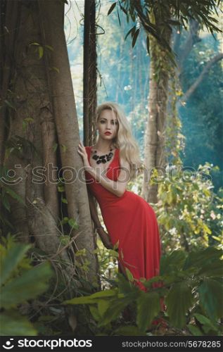 Young beautiful lady in red dress in tropical forest