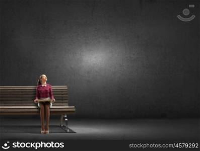 Young beautiful lady sitting on bench and reading book