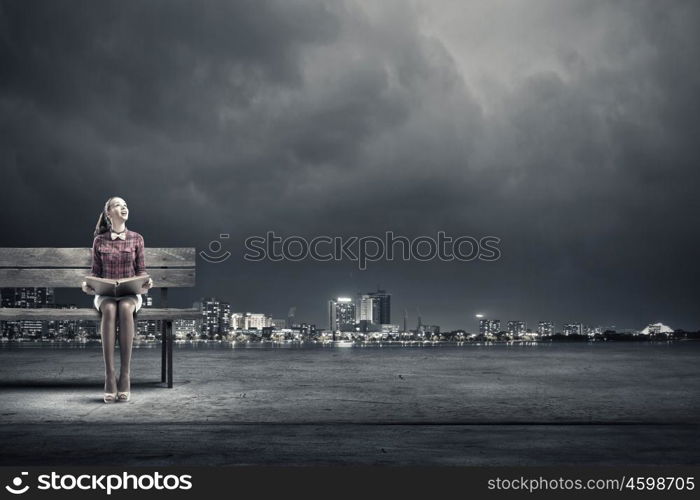 Young beautiful lady sitting on bench and reading book