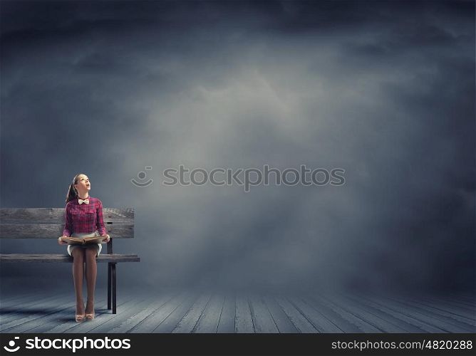Young beautiful lady sitting on bench and reading book