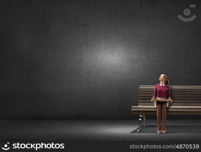 Young beautiful lady sitting on bench and reading book