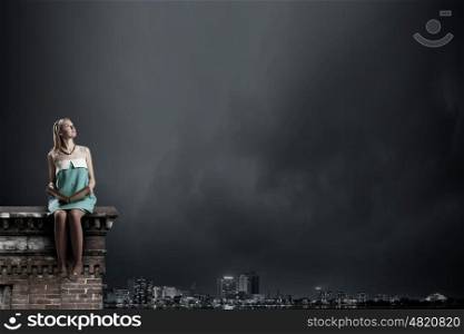 Young beautiful lady sitting on roof with book in hands. Girl with book