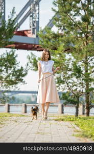 Young beautiful lady walking with her dog on lead in summer park