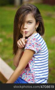 Young beautiful Little girl has put forefinger to lips as sign of silence, outdoors summer