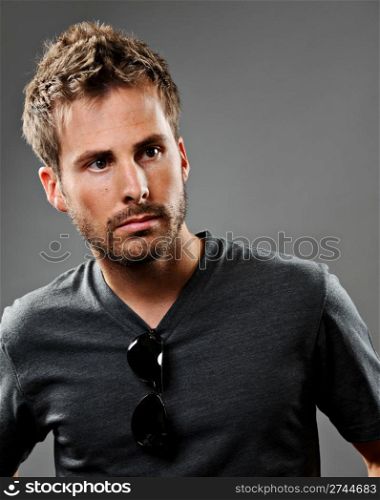Young beautiful male model wearing a gray t-shirt. He has a serious expression and is shot on a gray background.