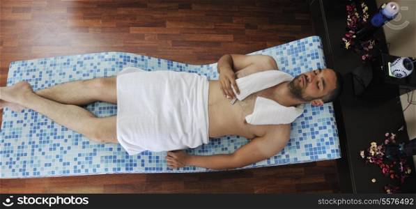 young beautiful man relaxing at spa and wellness center at hot bed with blue tiles decoration
