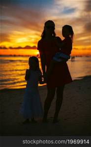 Young beautiful mother and her adorable little daughters on the beach at sunset. Beautiful mother and daughter on the beach enjoy sunset view