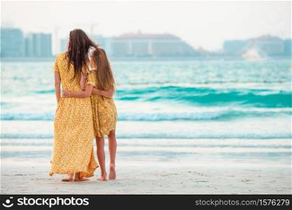 Young beautiful mother and her little daughter on the beach on the dawn time. Beautiful mother and daughter at the beach enjoying summer vacation.
