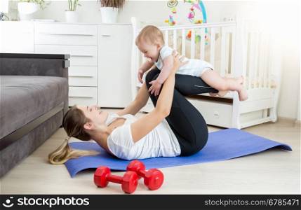 Young beautiful mother doing yoga exercise with her baby on floor at living room