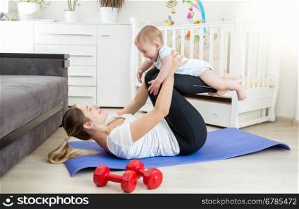 Young beautiful mother doing yoga exercise with her baby on floor at living room